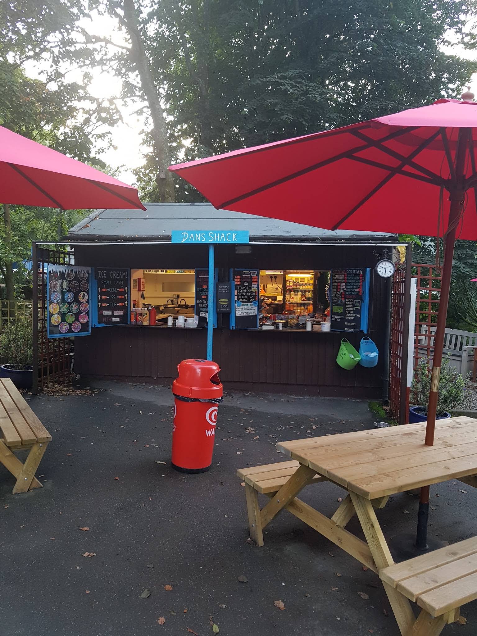 The complete Dan’s Shack hut and blue sign, with red parasols and picnic tables, photographed in September 2017