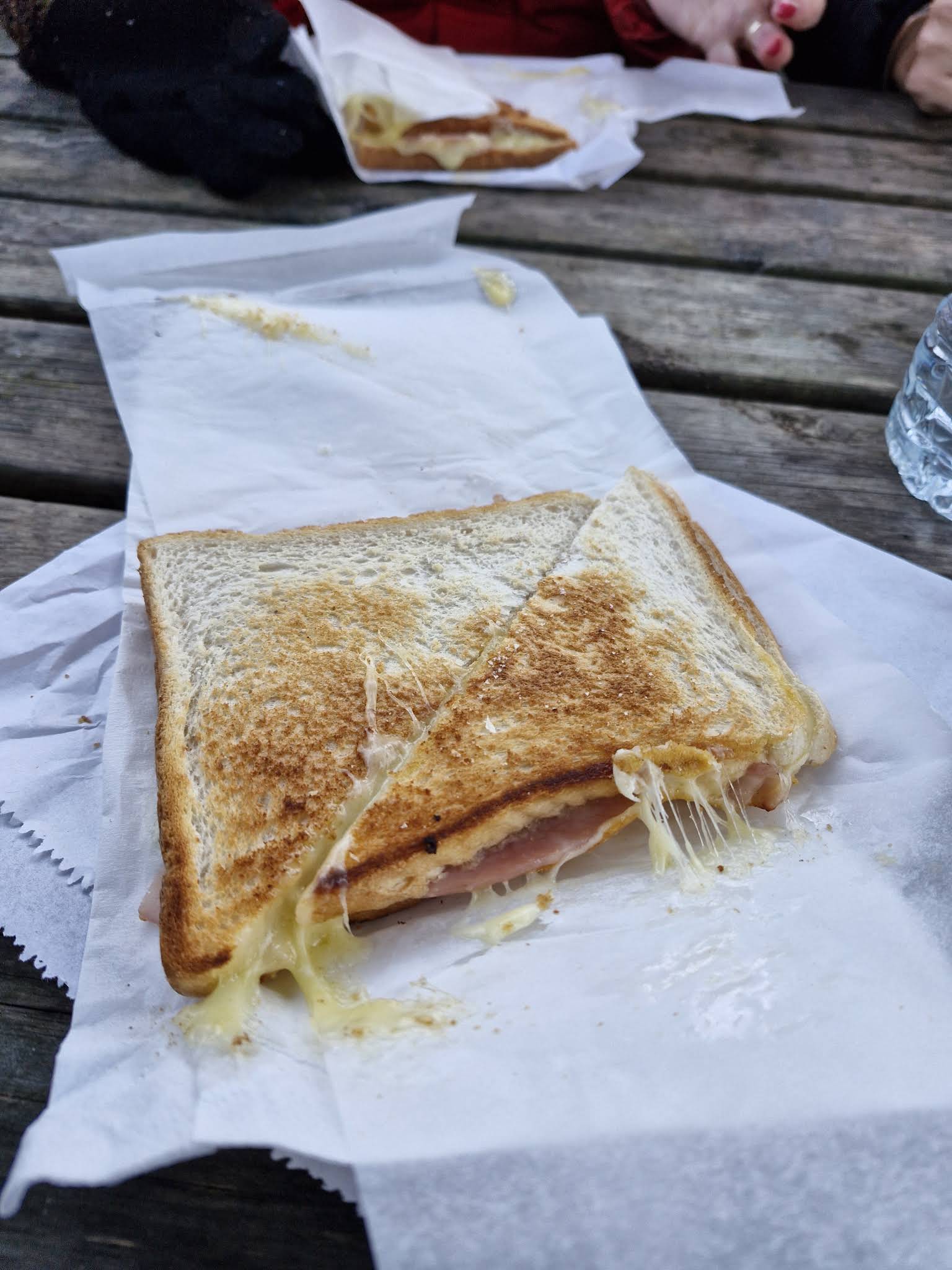 A whole ham and cheese toastie in paper on a picnic table at Dan’s Shack